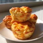 A stack of four golden brown, fluffy egg bites with browned cheese tops served on a white plate.