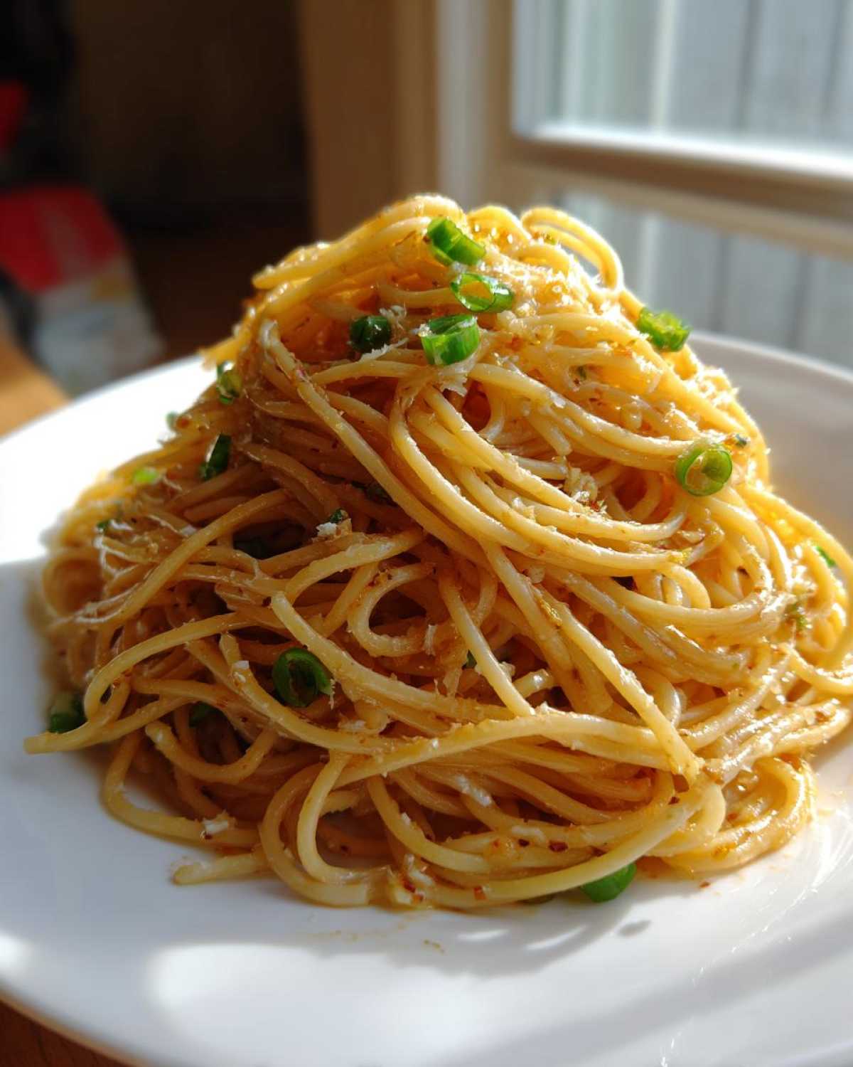 A mound of glossy, saucy garlic noodles topped with chopped green onions and grated cheese, served on a white plate.