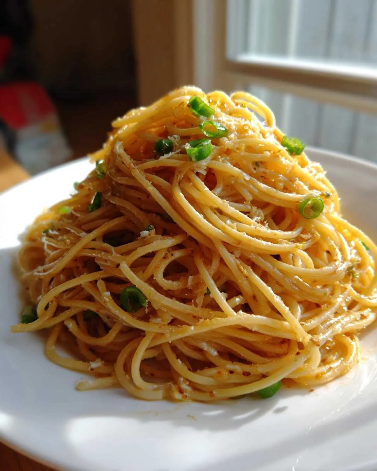 A mound of glossy, saucy garlic noodles topped with chopped green onions and grated cheese, served on a white plate.