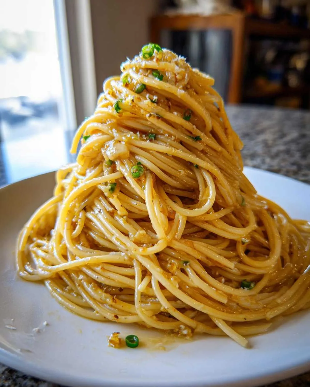 A tall, dramatic mound of glossy garlic noodles tossed in a rich sauce and topped with green onions.