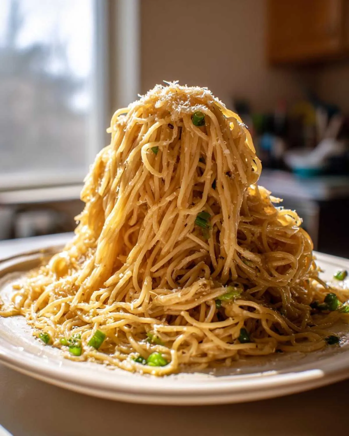 A tall, dramatic mound of saucy garlic noodles topped with grated cheese and green onions.