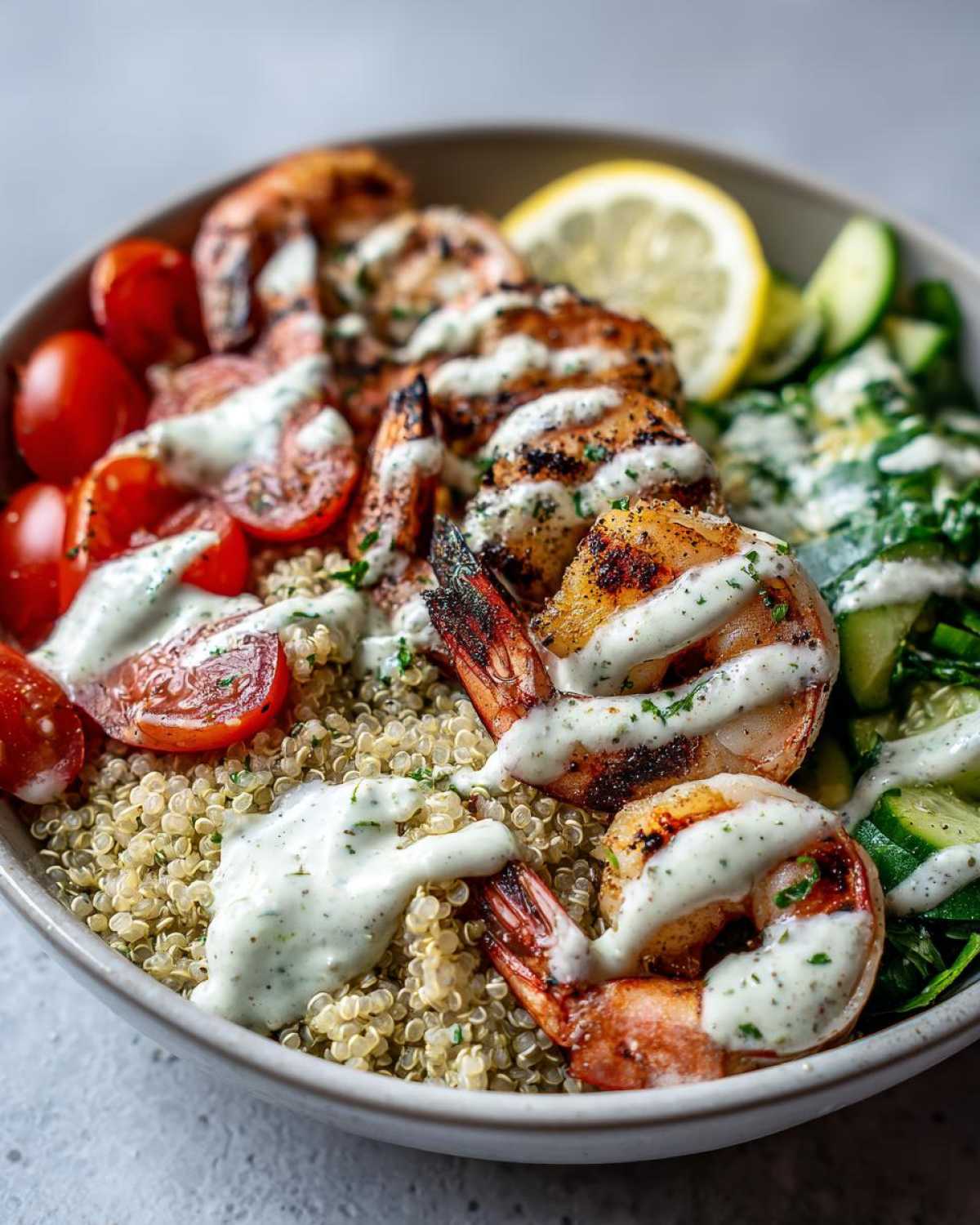 Close-up of a vibrant grilled shrimp bowl featuring grilled shrimp, quinoa, cherry tomatoes, cucumbers, and a creamy herb dressing.