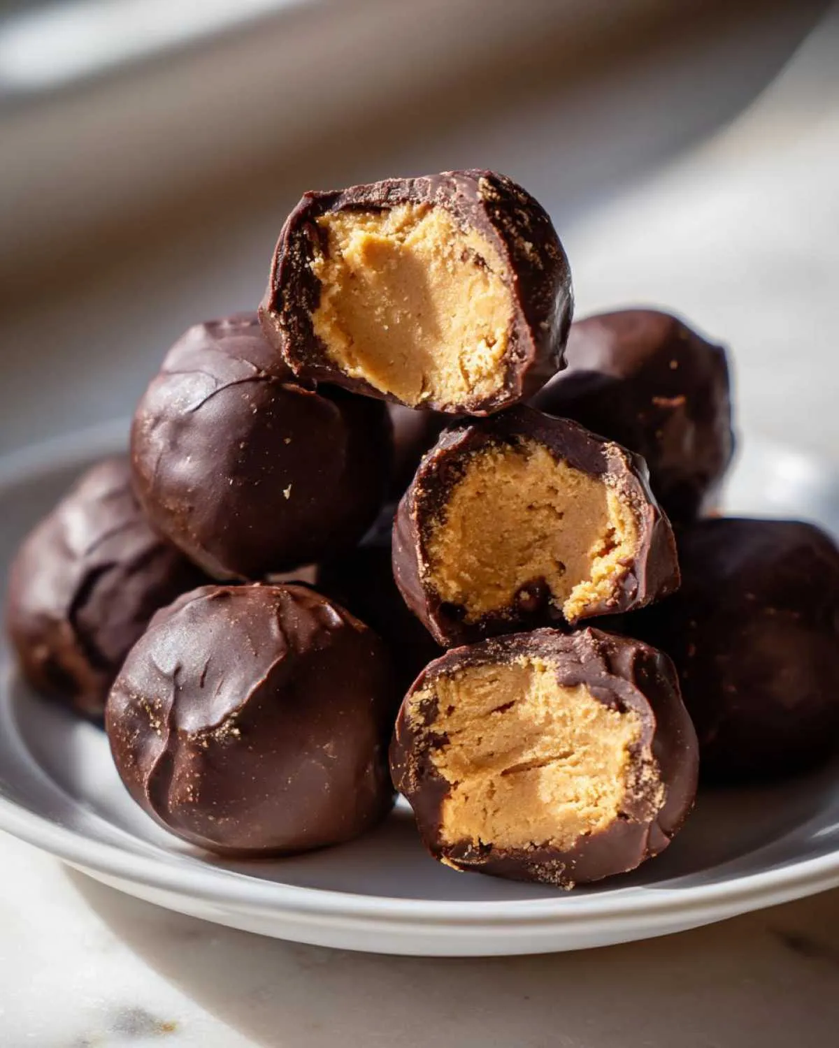 A stack of rich chocolate covered peanut butter balls, with two cut in half showing the creamy peanut butter filling.