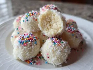 A pile of white chocolate-coated sugar cookie truffles rolled in coconut and colorful sprinkles.