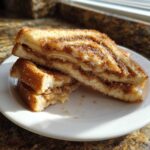 Two halves of a grilled Amish cinnamon flop sandwich stacked on a white plate, showing gooey brown sugar filling.
