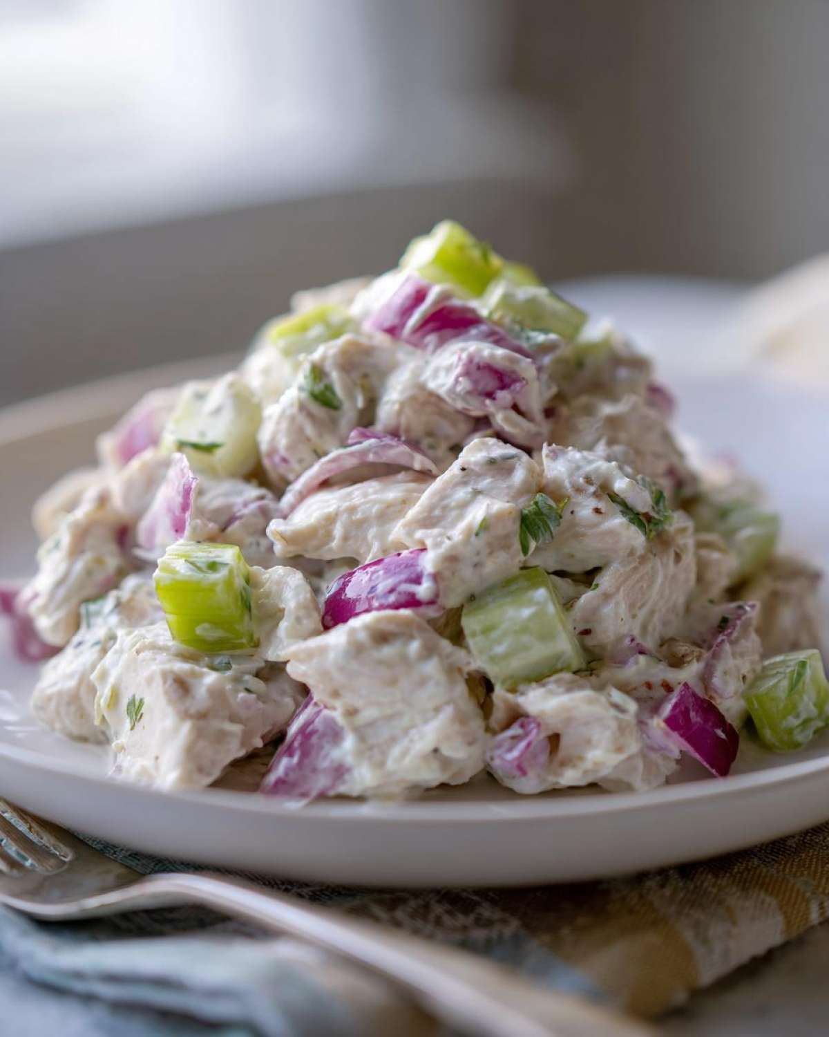 A mound of creamy baked marinated chicken salad featuring chunks of chicken, bright red onion, and celery on a white plate.