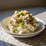 A close-up serving of creamy baked marinated chicken salad mixed with chunks of celery and red onion.