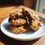 A stack of four moist banana bread chocolate chip cookies on a white plate, one broken open.
