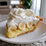 A perfect slice of banana cream pie recipe showing layers of crust, custard, banana slices, and whipped cream topping.