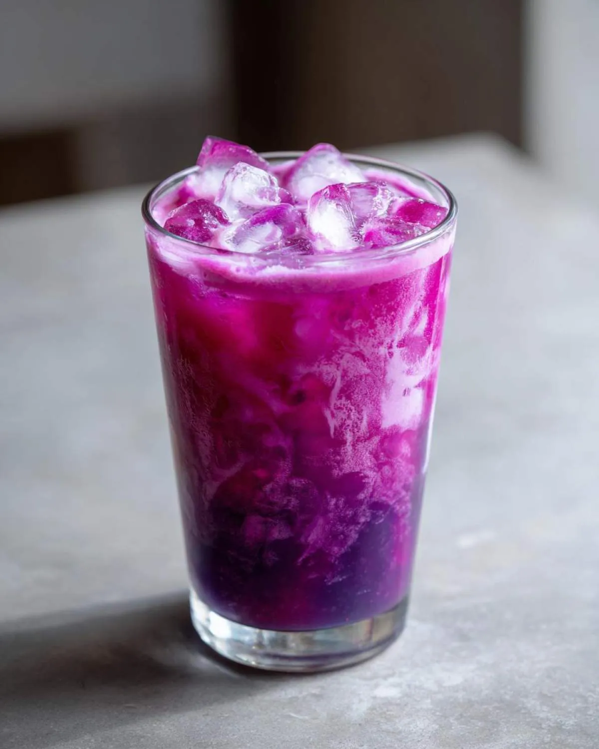 Close-up of a tall glass filled with a layered blackberry coconut pink drink and ice cubes.