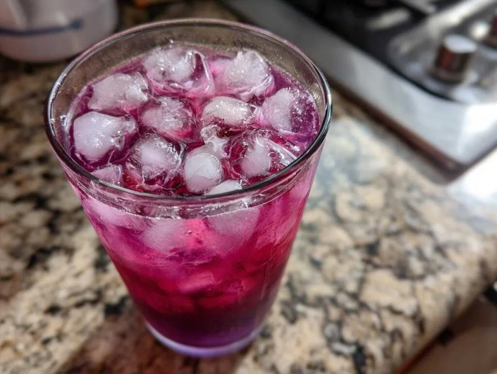 Close-up of a tall glass filled with a vibrant, layered blackberry coconut pink drink and plenty of ice cubes.