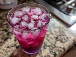 Close-up of a tall glass filled with a vibrant, layered blackberry coconut pink drink and plenty of ice cubes.