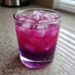 Close-up of a vibrant blackberry coconut pink drink layered with bright magenta and deep purple, filled with ice cubes.