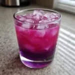 Close-up of a vibrant blackberry coconut pink drink layered with bright magenta and deep purple, filled with ice cubes.