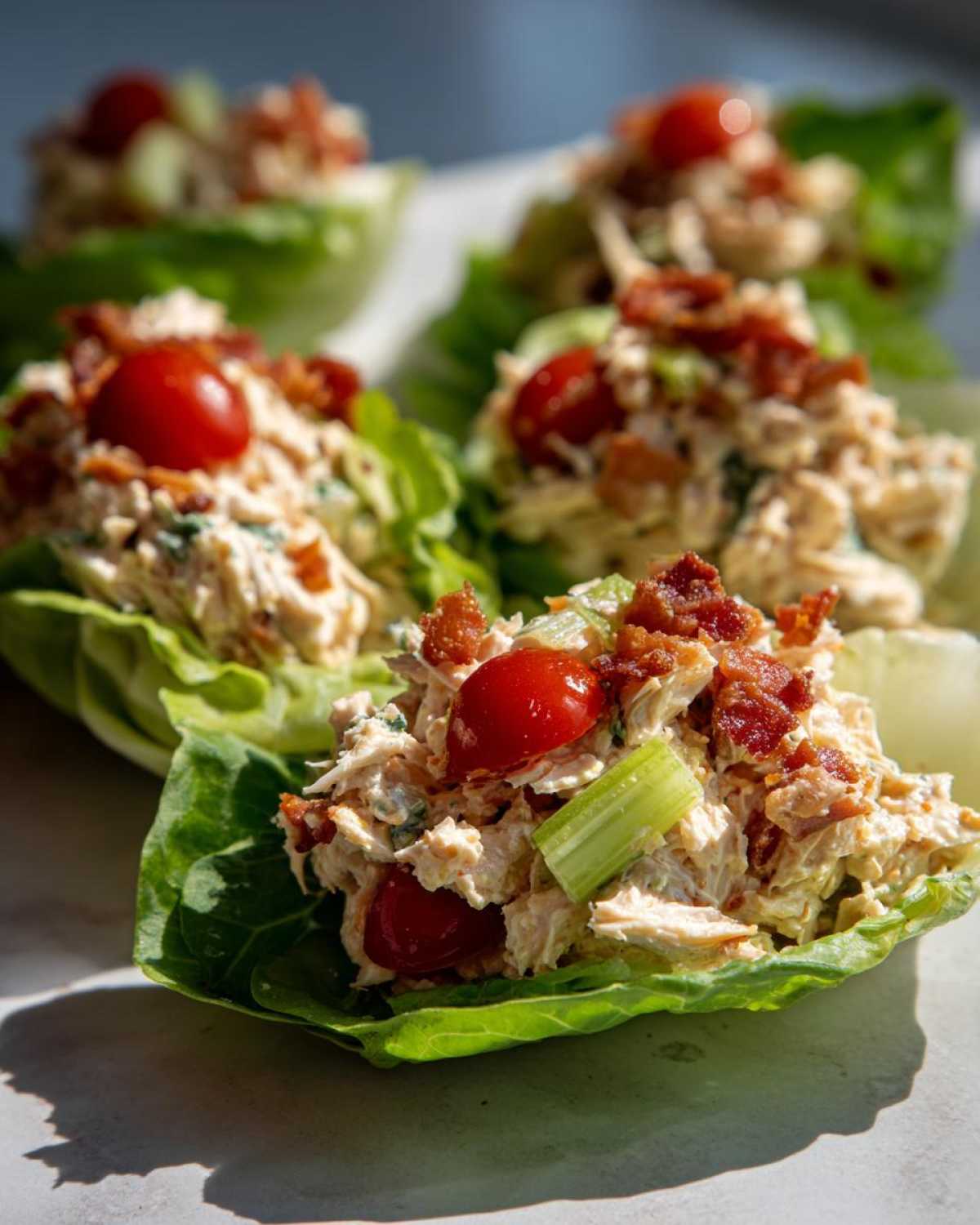Close-up of blt chicken salad served in crisp lettuce cups, topped with bacon and cherry tomatoes.