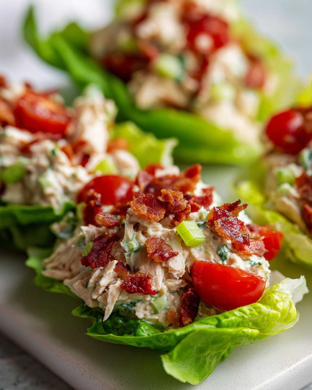 Close-up of blt chicken salad served in crisp lettuce cups, topped with bacon bits and cherry tomatoes.