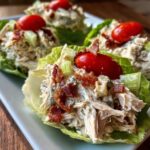 Close-up of blt chicken salad served in crisp lettuce cups, topped with bacon bits and a cherry tomato.