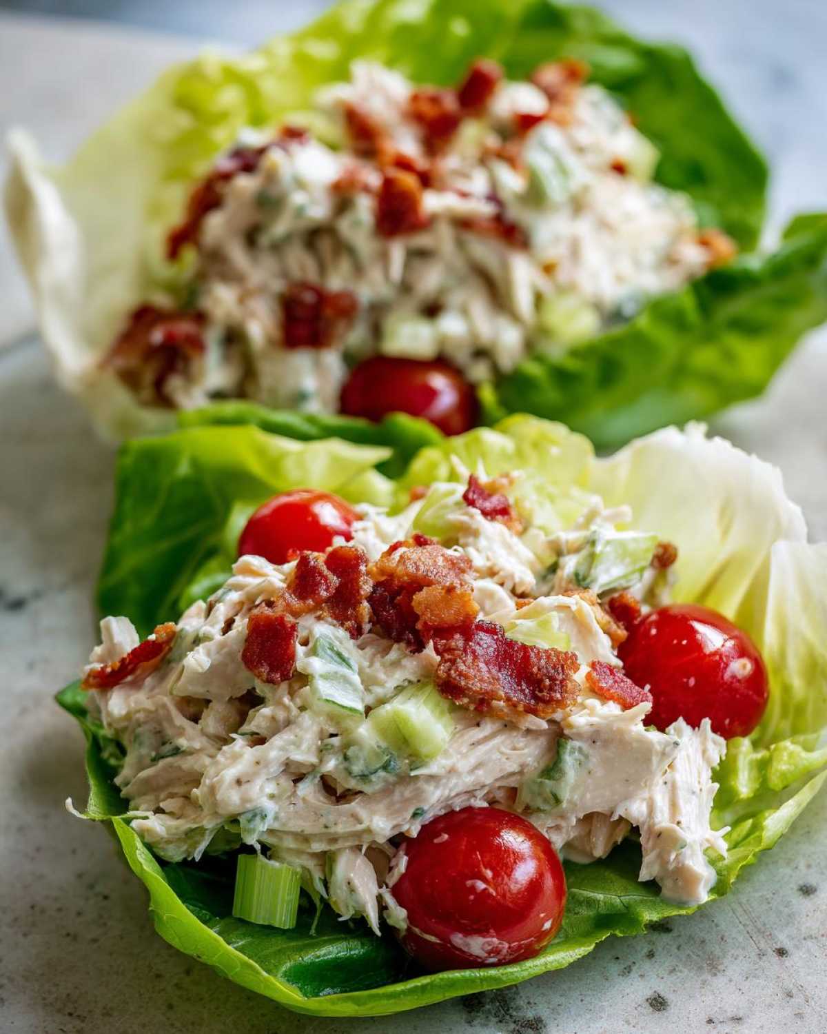 Close-up of blt chicken salad served in crisp lettuce cups, topped with bacon bits and cherry tomatoes.