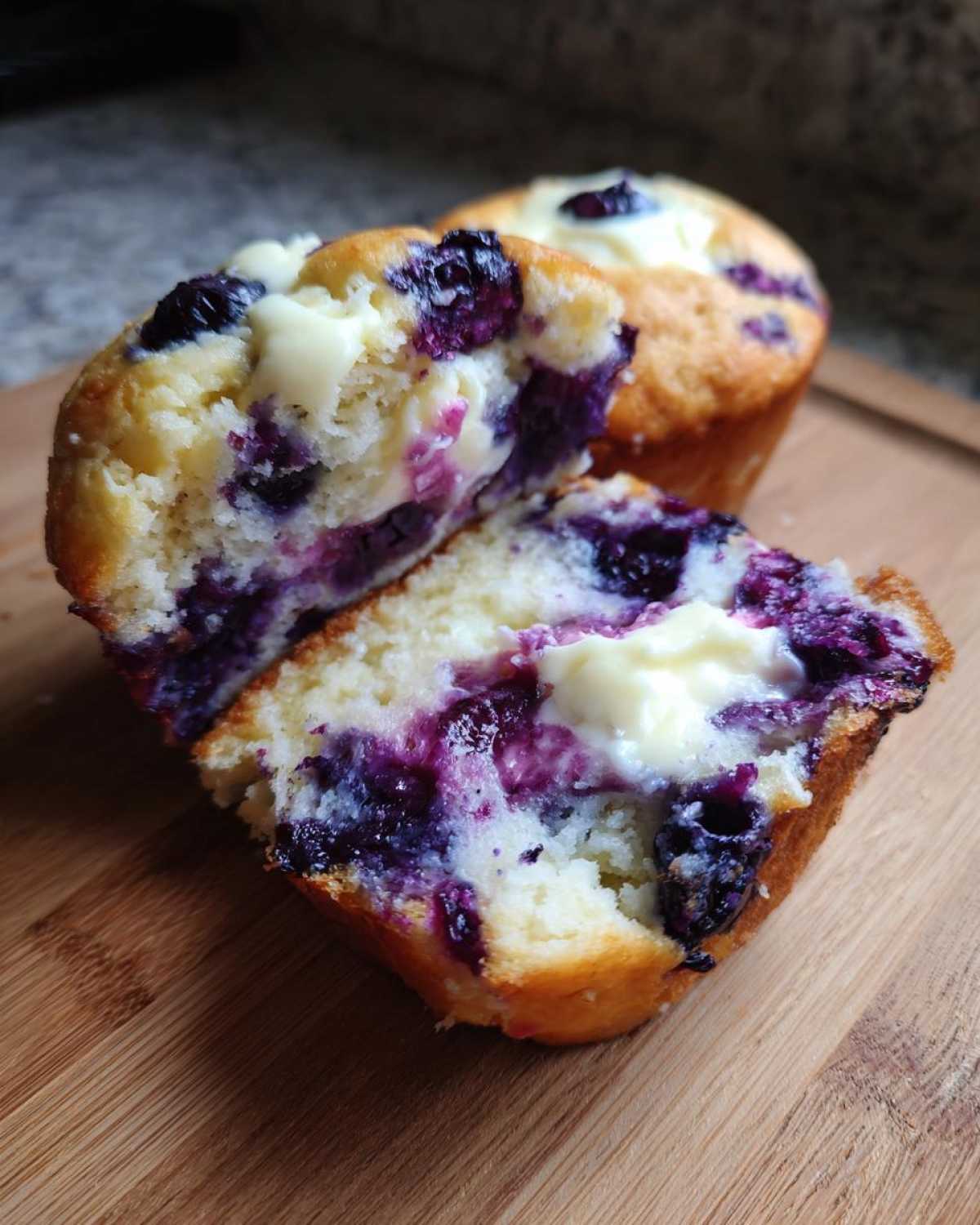 A blueberry cream cheese muffin cut in half showing the moist interior, bursting blueberries, and creamy filling.