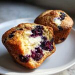 Close-up of a blueberry cream cheese muffin cut in half, showing the moist crumb, dark blueberries, and creamy filling.