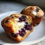 Close-up of a blueberry cream cheese muffin cut in half, showing the moist crumb, dark blueberries, and creamy filling.