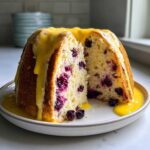 A slice cut from a blueberry lemon angel food cake, generously drizzled with bright yellow lemon glaze.