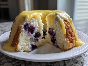 Cross-section view of a moist blueberry lemon angel food cake topped with a thick, bright yellow lemon glaze.