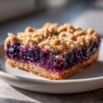 A close-up, appetizing shot of a single square of blueberry pie bars showing the thick, jammy blueberry filling and crumbly topping.