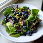 Close-up of a vibrant blueberry pistachio spring salad featuring mixed greens, fresh blueberries, chopped pistachios, and red onion slices.