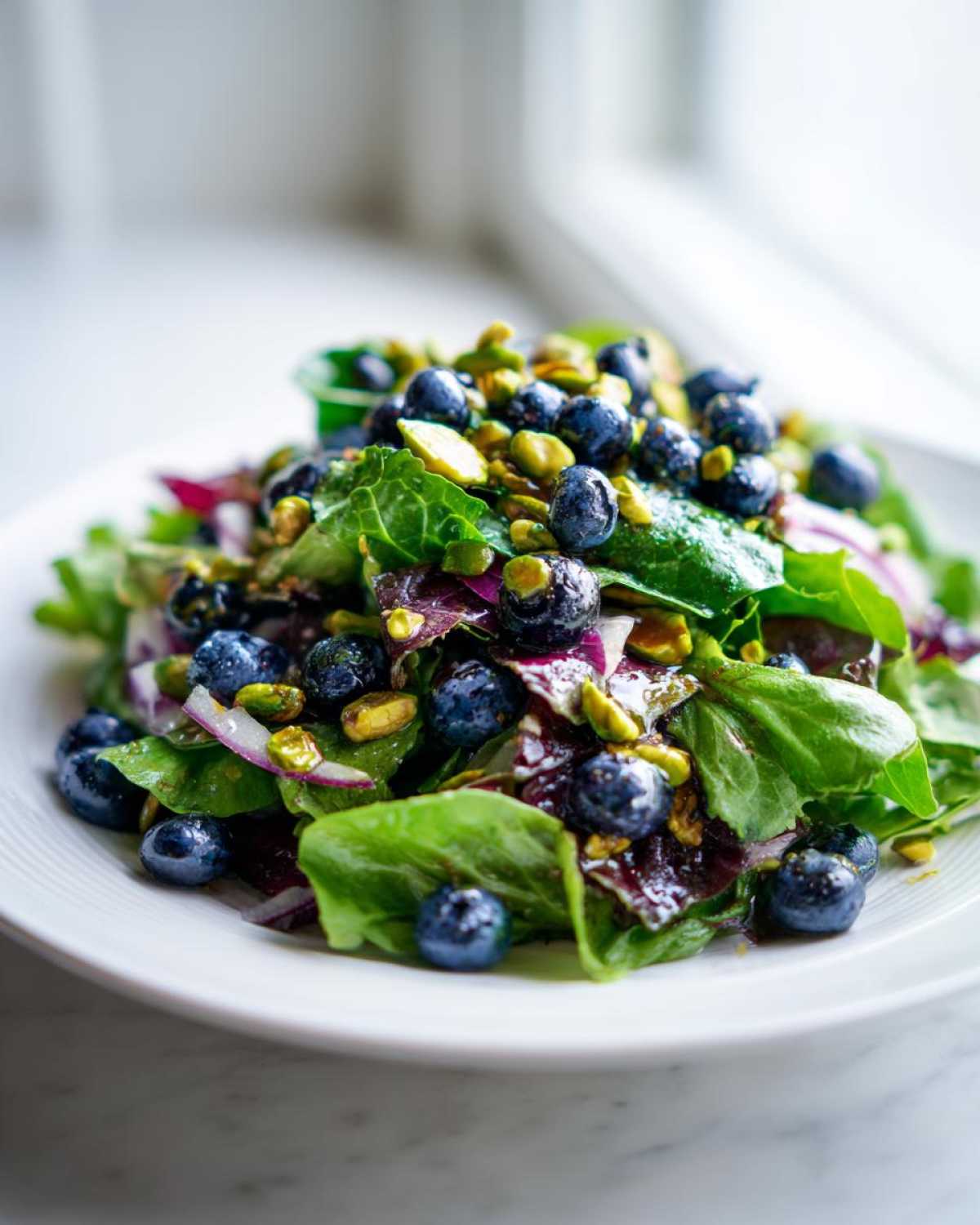 Close-up of a fresh blueberry pistachio spring salad featuring mixed greens, bright blueberries, and green pistachios.