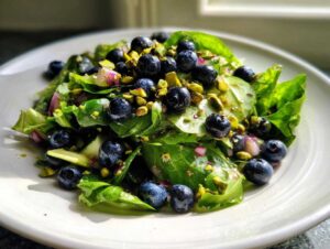 A close-up of a vibrant blueberry pistachio spring salad featuring fresh greens, whole blueberries, and chopped pistachios.