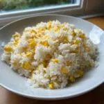 A white bowl filled with fluffy white rice mixed generously with bright yellow sweet corn kernels, representing buttered corn rice.
