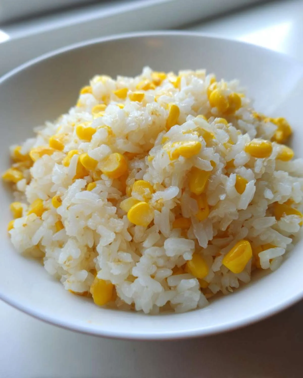 Close-up of fluffy white rice mixed generously with bright yellow sweet corn kernels, served in a white bowl, ready to eat buttered corn rice.