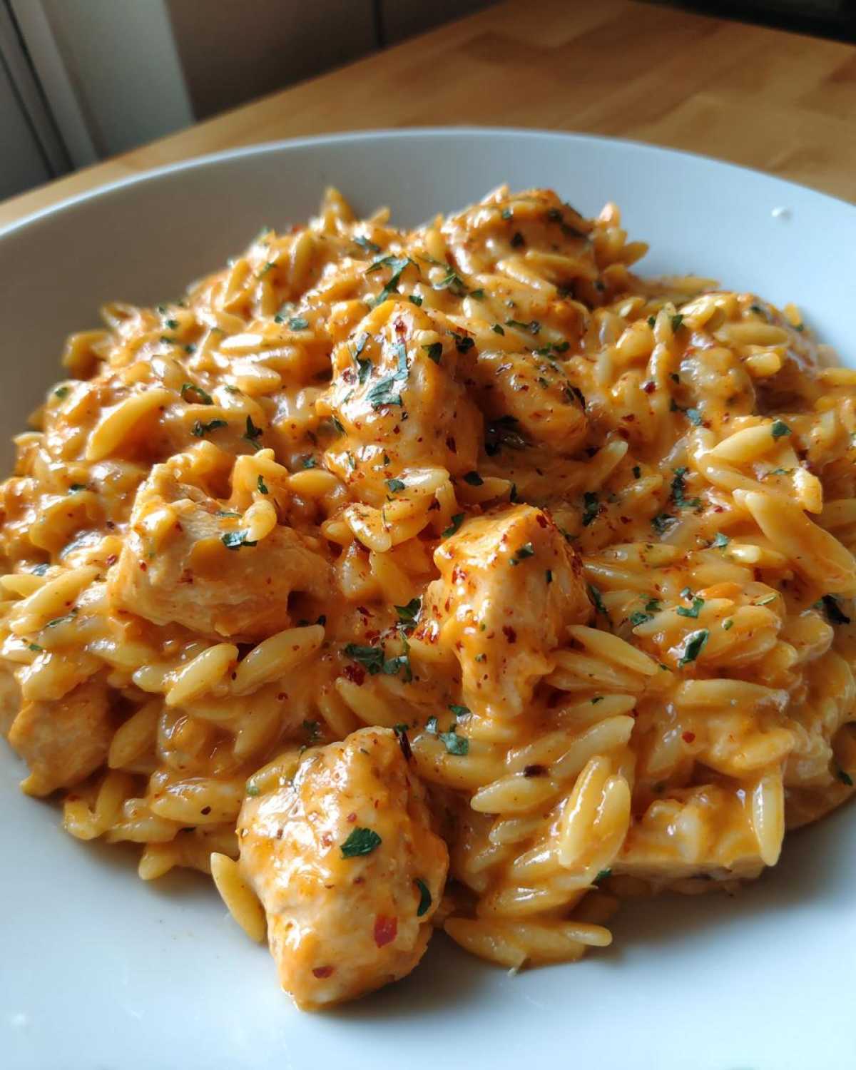 Close-up of a bowl filled with creamy cajun chicken alfredo orzo, garnished with parsley.