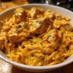 Close-up of a bowl filled with creamy Cajun chicken alfredo orzo, topped with herbs and chili flakes.