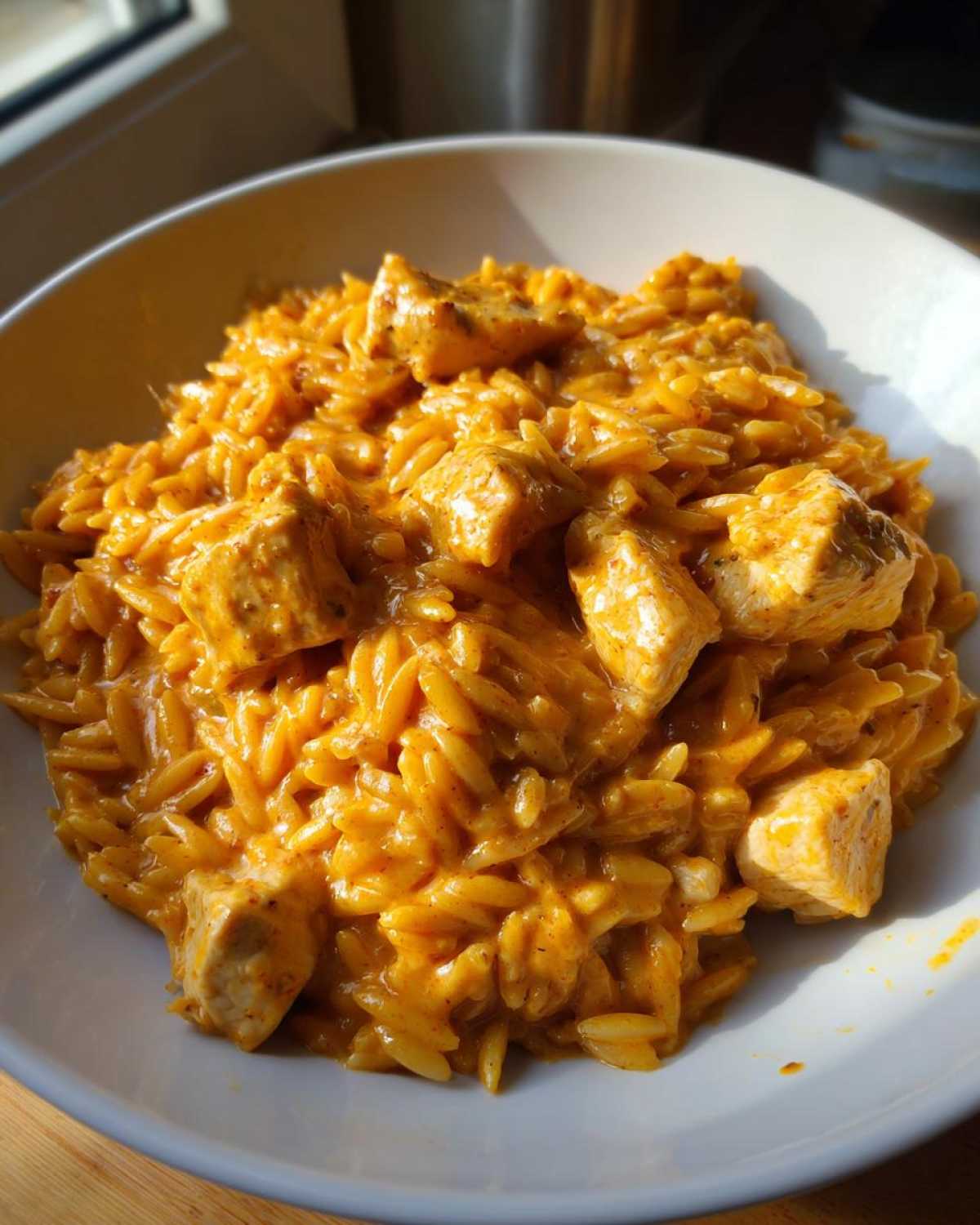 A close-up of creamy, orange-hued cajun chicken alfredo orzo topped with chunks of seasoned chicken.