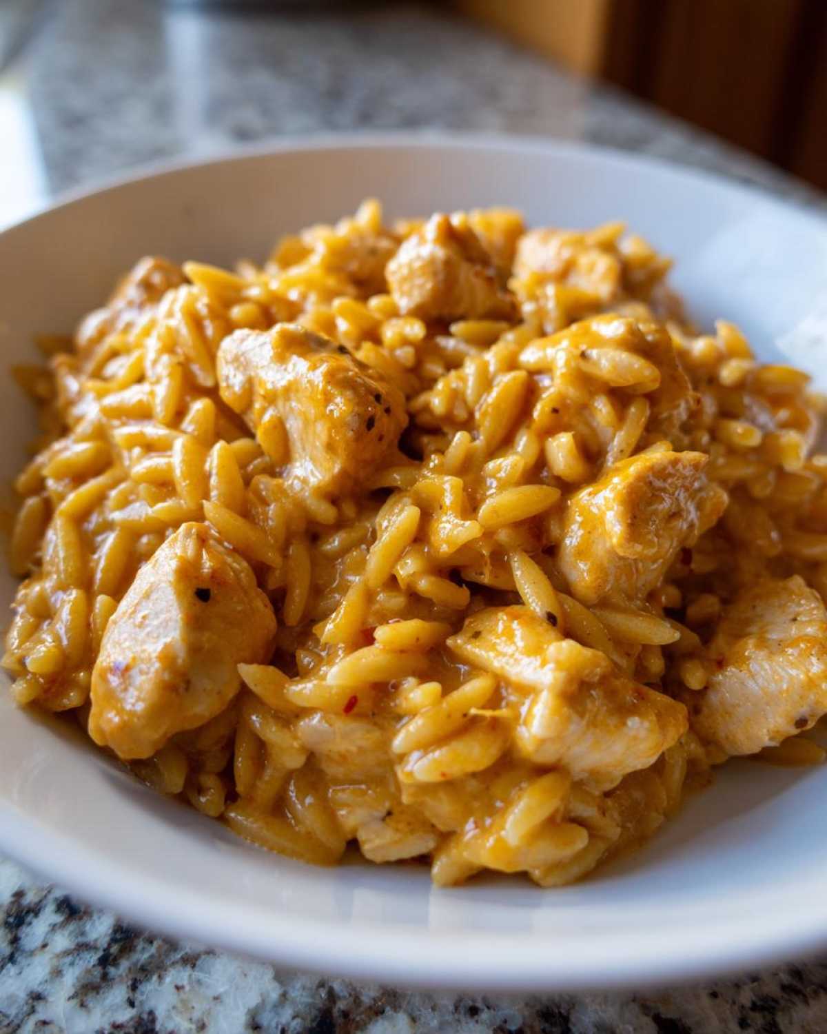 Close-up of creamy cajun chicken alfredo orzo pasta mixed with chunks of seasoned chicken in a white bowl.