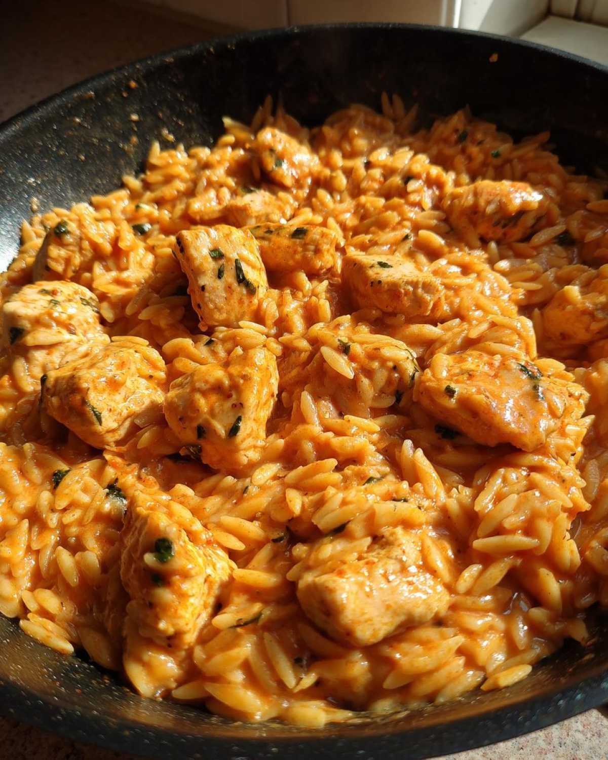 Close-up of creamy cajun chicken alfredo orzo mixed with chunks of seasoned chicken in a dark skillet.