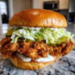 A close-up of a cajun crispy chicken sandwich with garlic sauce, pickles, and shredded lettuce on a brioche bun.