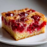 A close-up of a square slice of moist cherry pineapple dump cake on a white plate.