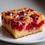 A close-up of a square slice of moist cherry pineapple dump cake on a white plate.