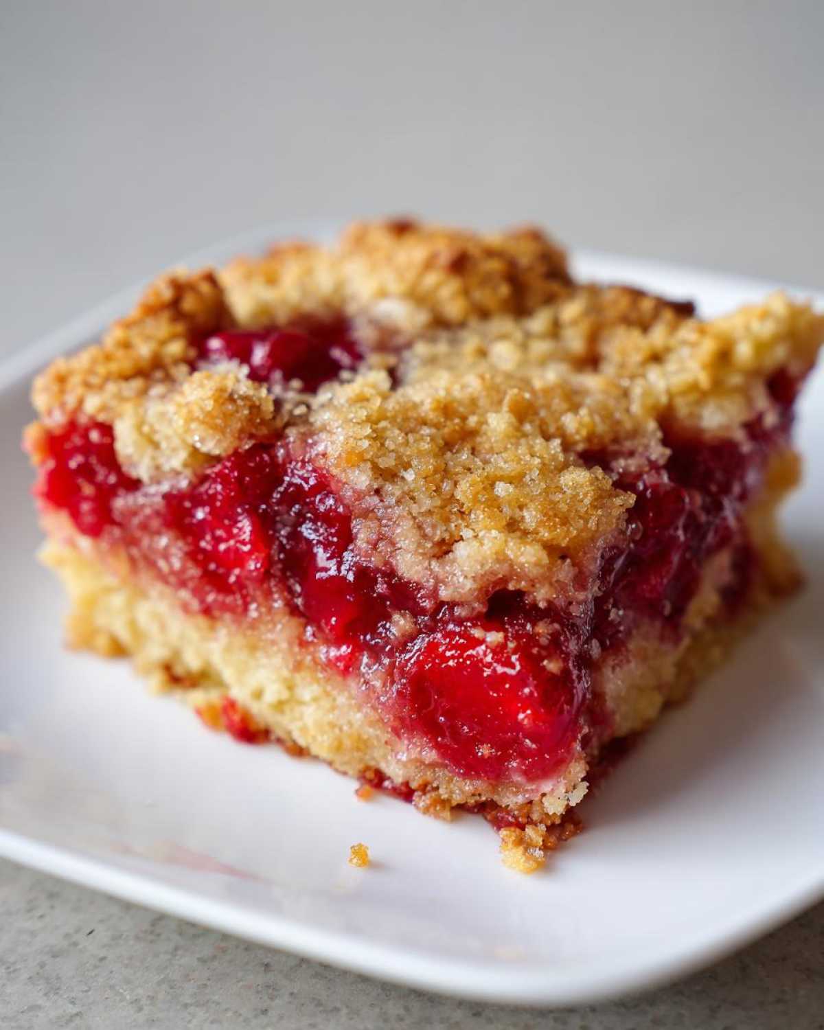 Close-up of a square slice of cherry pineapple dump cake showing the bright red cherry filling and golden crumb topping.