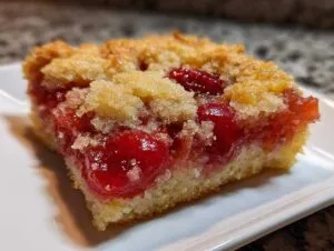 Close-up of a moist square slice of cherry pineapple dump cake showing bright red cherries and a golden crumb topping.