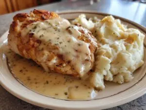 A golden-brown chicken breast covered in creamy chicken and garlic gravy served next to fluffy cheesy mashed potatoes.