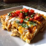 A close-up serving of cheesy chicken burrito casserole topped with fresh diced tomatoes and cilantro.