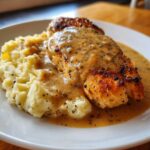 A perfectly cooked chicken breast smothered in rich chicken and garlic gravy next to cheesy mashed potatoes.