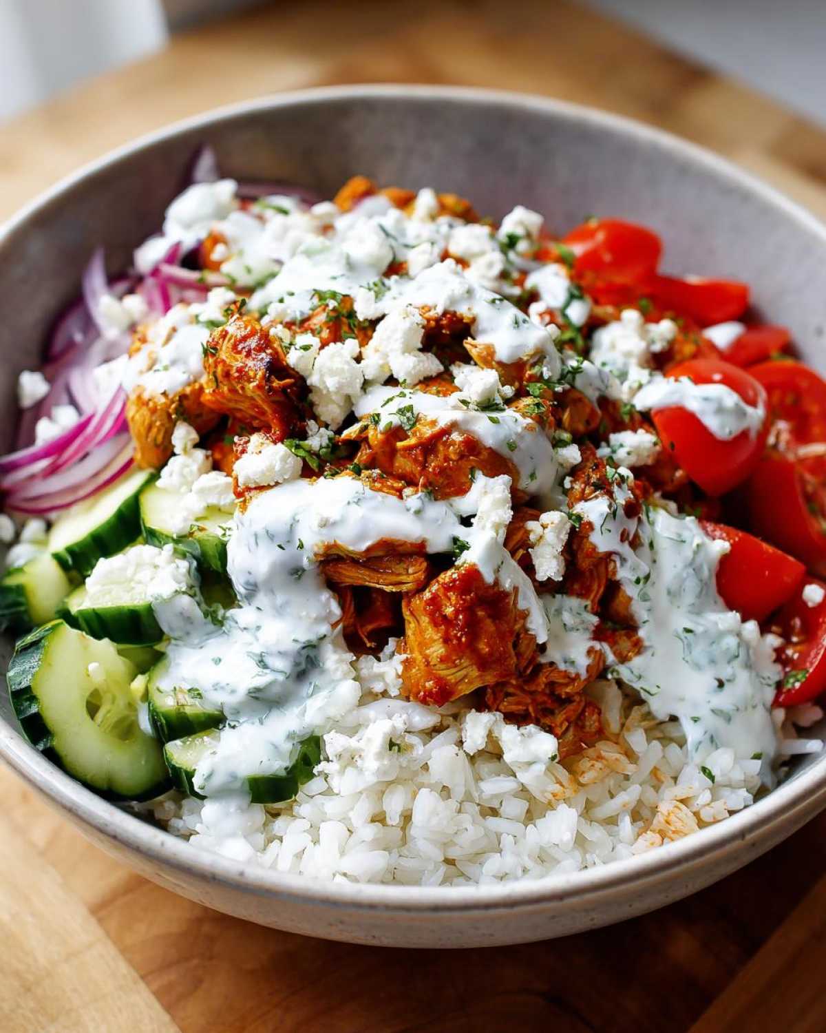 Close-up of a bowl filled with rice, seasoned chicken, cucumbers, tomatoes, feta, and drizzled with tzatziki sauce, showcasing a delicious chicken gyro bowls serving.