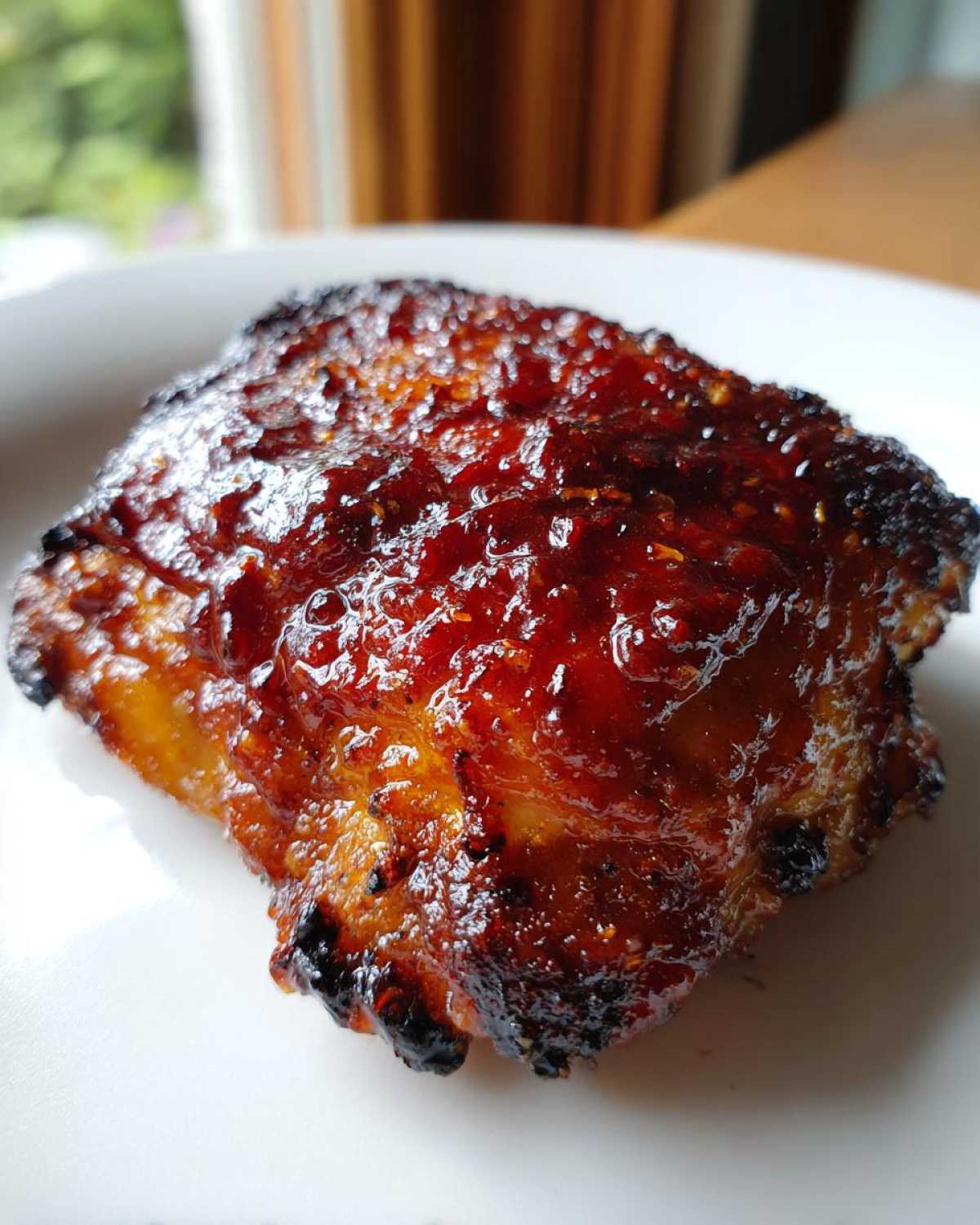 Close-up of a perfectly cooked chipotle honey chicken thigh with a shiny, dark red glaze.