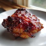 Close-up of a perfectly cooked chipotle honey chicken thigh with a thick, caramelized, glossy glaze.