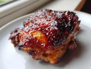 Close-up of a perfectly glazed, caramelized chipotle honey chicken thighs piece on a white plate.